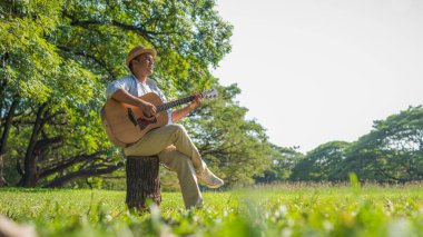 Genç Asyalı adam parkta gitar çalıyor.