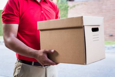 Paket karton kutulu kırmızı üniformalı teslimatçı.