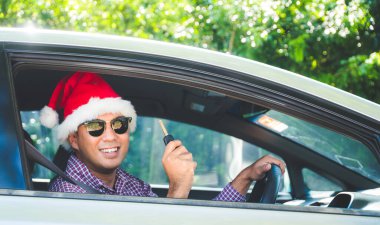 Genç Asyalı adam Noel temalı arabada otururken arabanın anahtarını tutuyor..