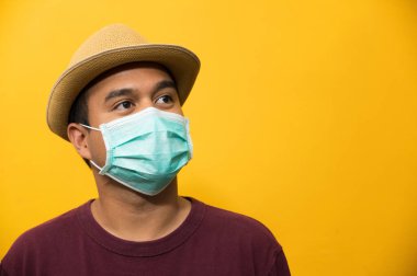 Korunaklı yüz maskesi takan Asyalı genç adamı sarı arka planda koronavirüse karşı kapatın..