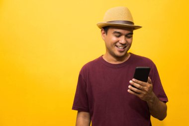 Asyalı adam sarı arka plandaki akıllı telefonundan memnun. Genç adam akıllı telefona bakıyor..