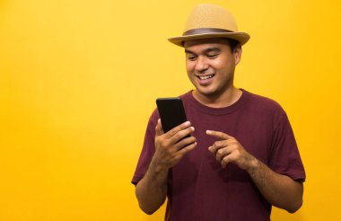 Asyalı adam sarı arka plandaki akıllı telefonundan memnun. Genç adam akıllı telefona bakıyor..