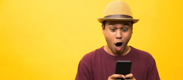 Asyalı adam sarı arka plandaki akıllı telefonundan memnun. Genç adam akıllı telefona bakıyor..