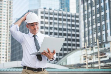 İnşaat mühendisliği inşaat alanında çalışırken dizüstü bilgisayar kullanıyor ve işiyle ilgili kötü hissediyor..