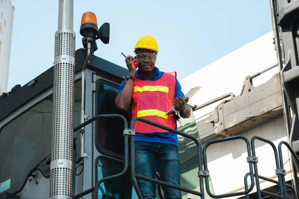 Black foreman worker working control the crane and forklift at Container cargo harbor to loading containers. African dock male staff with radio walkie-talkie for Logistics import export shipping concept.