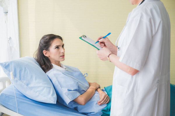 Senior woman doctor and patient discussing and making notes about symptom problem while she lay down on the bed.