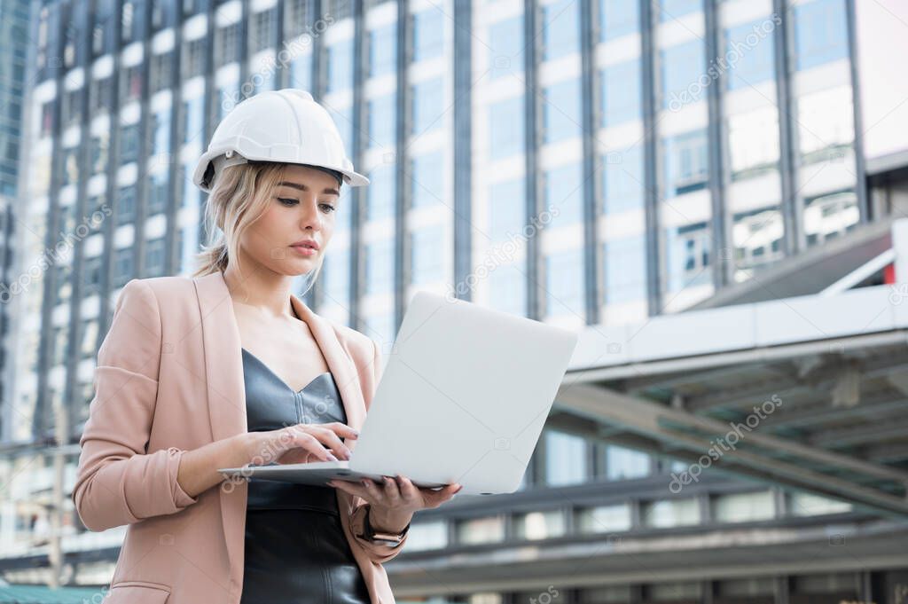 Portrait of pretty young civil engineer woman working planning project with laptop on construction building background. Evolution construction concept.