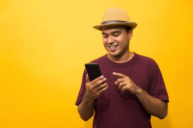 Asyalı adam sarı arka plandaki akıllı telefonundan memnun. Genç adam akıllı telefona bakıyor..