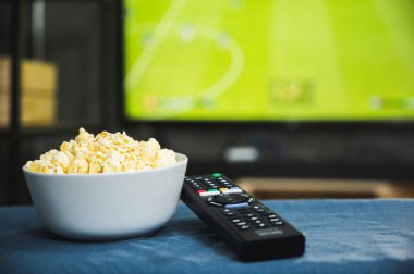 Futbol programının arka planında patlamış mısır ve televizyon uzaktan kumandası. Televizyon izlemek rahatlama konsepti.