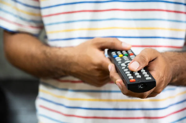 Young man holding television remote control. Hands pointing to tv set and turning it on or off select channel watching tv on his sofa at home in the living room relax.