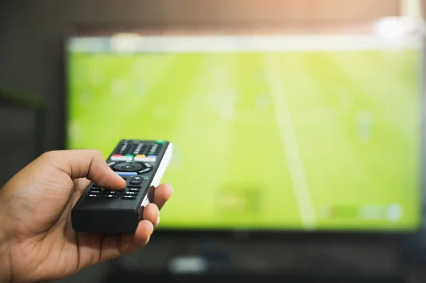 Young man holding television remote control watching football program. Hands pointing to tv screen set and turning it on or off select channel watching tv in the living room relax.