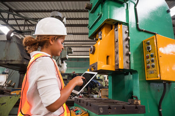 Female industrial worker working and checking machine in a large industrial factory with many equipment.