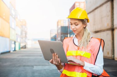 Ustabaşı kadın işçi konteyner kargo limanında kontrol ediyor dizüstü bilgisayarla konteynırları yüklüyor. Rıhtım kadın personel lojistik ithalat ihracat nakliye kavramı.