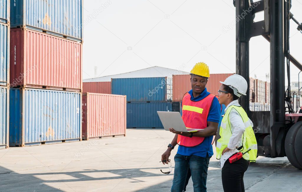 Two Black foreman man & woman worker working checking at Container cargo harbor holding laptop computer and using walkie-talkie to loading containers. African dock male and female staff business Logistics import export shipping concept.