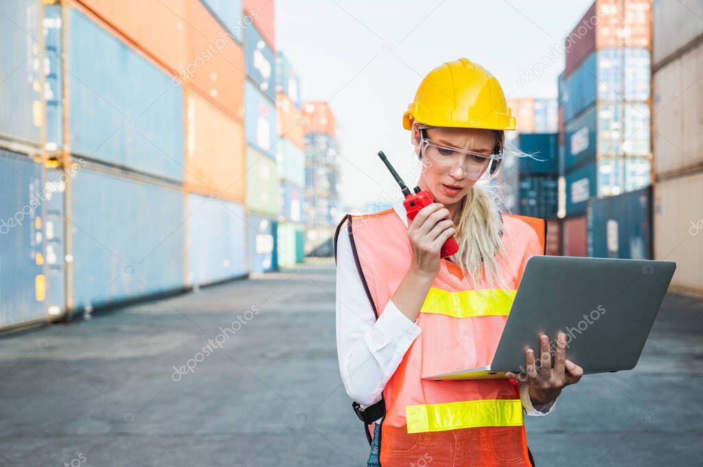 Foreman woman worker working checking at Container cargo harbor holding laptop computer and radio walkie-talkie to loading containers. Dock female staff business Logistics import export shipping concept.