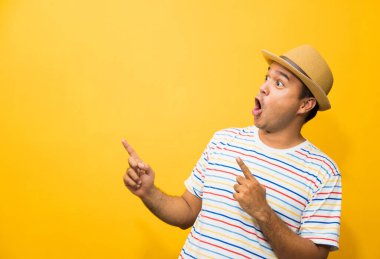 Genç mutlu & komik Asyalı adam sarı arkaplandaki metin için boş alanı işaret ediyor.