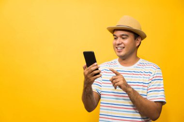 Asyalı adam sarı arka plandaki akıllı telefonundan memnun. Genç adam akıllı telefona bakıyor..