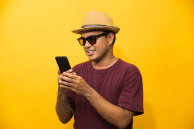 Asyalı adam sarı arka plandaki akıllı telefonundan memnun. Genç adam akıllı telefona bakıyor..