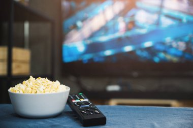 Televizyonun arka planında patlamış mısır ve televizyon uzaktan kumandası. Televizyon izlemek rahatlama konsepti.