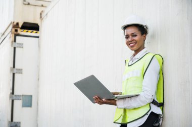 Kara ustabaşı kadın işçi konteynır kargo limanında kontrol ediyor dizüstü bilgisayarla konteynırları yüklüyor. Afrika rıhtımı kadın personel lojistik ithalat ihracat konsepti.