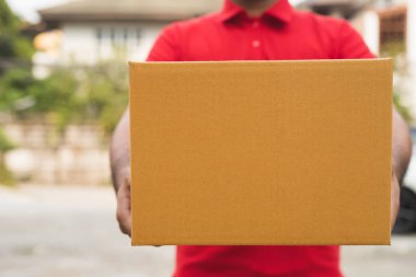 Kırmızı üniformalı postacı elinde bir paket tutuyor..