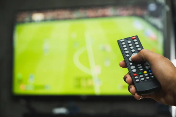 Young man holding television remote control watching football program. Hands pointing to tv screen set and turning it on or off select channel watching tv in the living room relax.