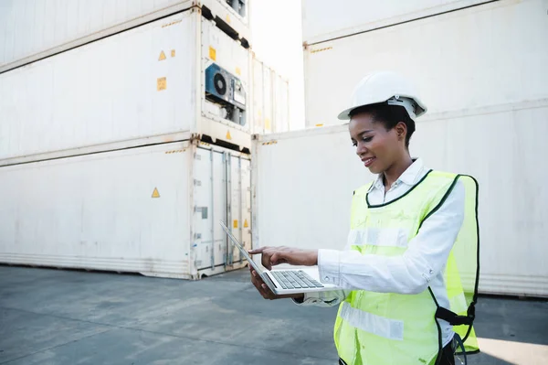 Black foreman woman worker working checking at Container cargo harbor holding laptop computer to loading containers. African dock female staff business Logistics import export shipping concept.