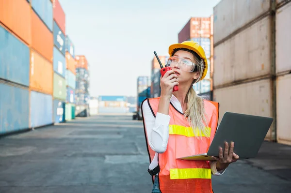 Foreman woman worker working checking at Container cargo harbor holding laptop computer and radio walkie-talkie to loading containers. Dock female staff business Logistics import export shipping concept.