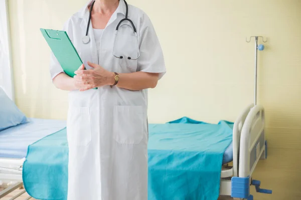 Senior woman doctor with clipboard standing near patient bed. Medical healthcare and doctor service in hospital.