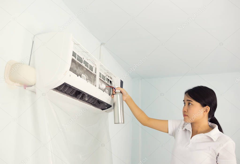 Woman cleaning air conditioner by foam cleaning agent.