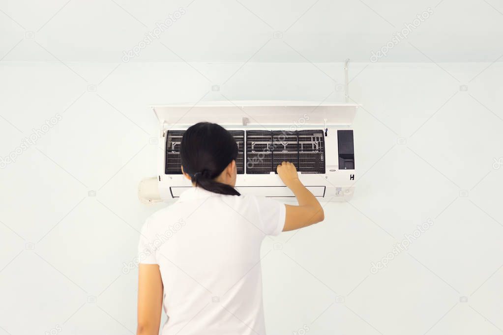 Woman checking air conditioner inside room.