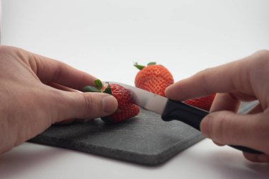 Çilek kesmek. Bir bıçak gözleniyor ve kesme tahtasının üzerinde çilekler kesiliyor..