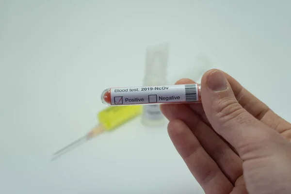 Ön planda koronavirüsün kan testi var. Kan tüpü 2019-NcOv 'dan önce pozitif çıktı. Arka planda Coronavirus aşısı bir şırınganın yanında..