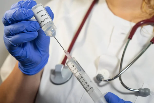 Nurse introducing the coronavirus vaccine into a syringe. The syringe has the 2019-NcOv vaccine. the nurse wears blue gloves and a mask.