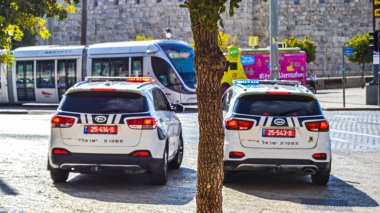 Ön planda iki polis arabası var. Arka planda Kudüs şehrinden geçen tramvay var. Seyahat etmek için çok güvenli bir şehir.