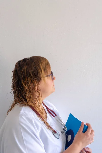 Female medical student. She\'s holding medical textbooks in her arms. She\'s dressed in a doctor\'s uniform. She has a stethoscope around her neck.