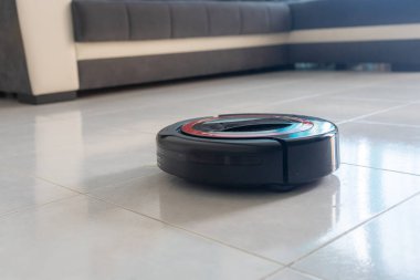 Robot elektrikli süpürge otomatik olarak zemini temizliyor. Arka planda bir kanepe var..