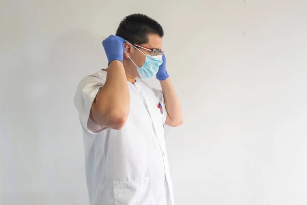 Doktor / hemşire koronavirüsten korunmak için maske takıyor. Mavi eldiven ve gözlük takıyor. Üniforması beyaz..