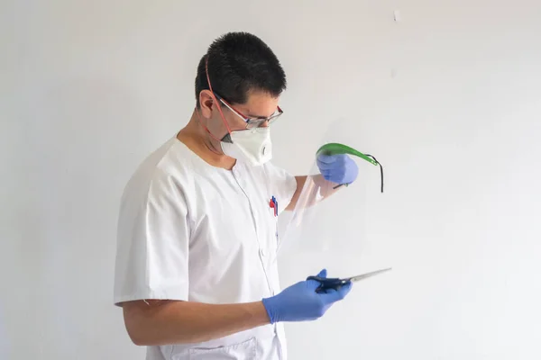 Doctor / nurse cutting a face shield with scissors to protect against the coronavirus. He is a young man. He wears gloves, masks, and glasses. He wears a white uniform.