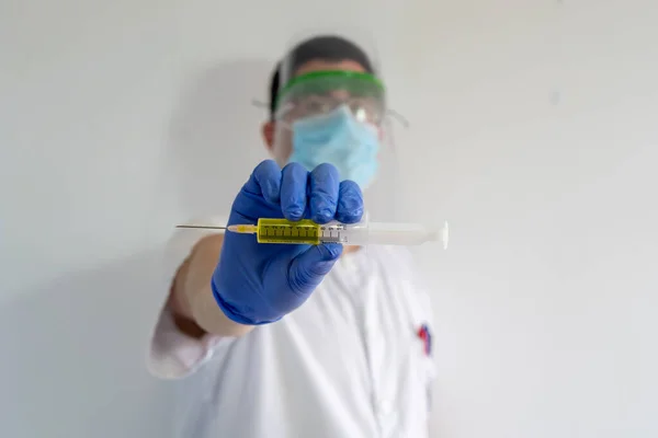 Doktor / Hemşire ve yüz kalkanı koronavirüs aşısını gösteriyor. Elinde aşıyı ve şırıngayı tutuyor. Beyaz bir üniforma giyiyor, maske, eldiven ve gözlük takıyor..