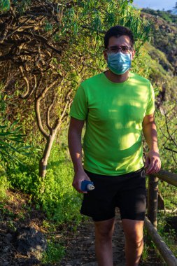 Koşucu ormanda koşmak için koşuyor. Elinde bir maske ve yumuşak bir matara var..