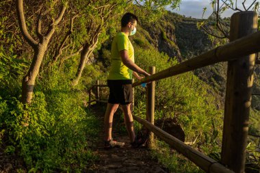 Koşucu baldırını geriyor. Adam bir ormandaymış ve bacağını korkuluklara dayamış. Elinde bir maske ve yumuşak bir matara var..