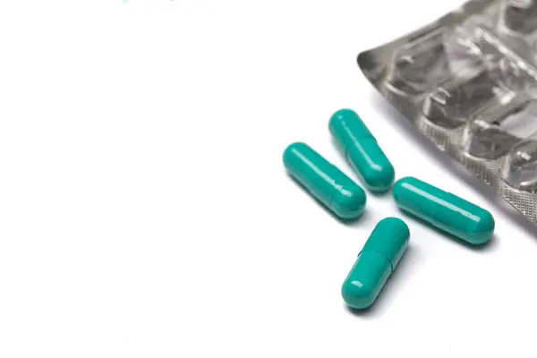 Зелені таблетки в капсулах на білому столі . — стокове фото