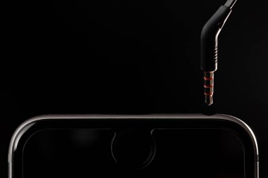 Siyah arka planda kulaklığı olmayan bir telefon.