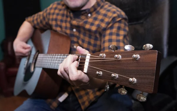 Guitarrista con camisa a cuadros toca acorde en guitarra