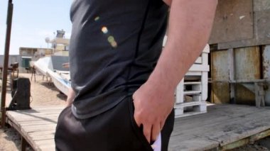 Adam deniz kenarında, kumsalda antrenman yapıyor, denize ve kuma bakıyor, boks yapıyor, koşuyor, telefonda konuşuyor, deniz taşı fırlatıyor.