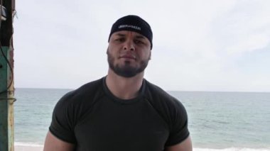 Adam deniz kenarında, kumsalda antrenman yapıyor, denize ve kuma bakıyor, boks yapıyor, koşuyor, telefonda konuşuyor, deniz taşı fırlatıyor.