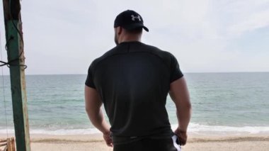 Adam deniz kenarında, kumsalda antrenman yapıyor, denize ve kuma bakıyor, boks yapıyor, koşuyor, telefonda konuşuyor, deniz taşı fırlatıyor.