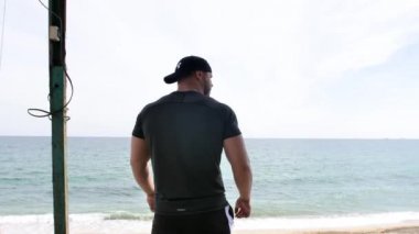 Adam deniz kenarında, kumsalda antrenman yapıyor, denize ve kuma bakıyor, boks yapıyor, koşuyor, telefonda konuşuyor, deniz taşı fırlatıyor.