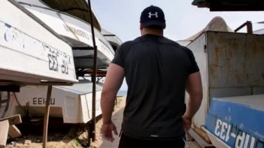 Adam deniz kenarında, kumsalda antrenman yapıyor, denize ve kuma bakıyor, boks yapıyor, koşuyor, telefonda konuşuyor, deniz taşı fırlatıyor.